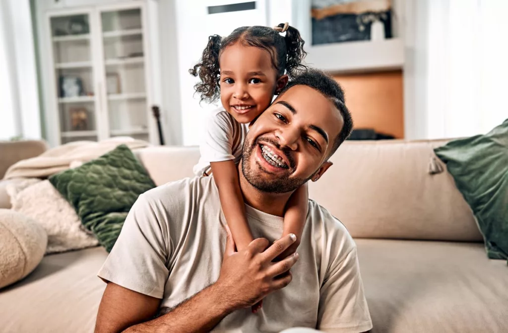 Un père souriant portant sa fille sur son dos, illustrant le soutien et l'amour présents dans une famille monoparentale.