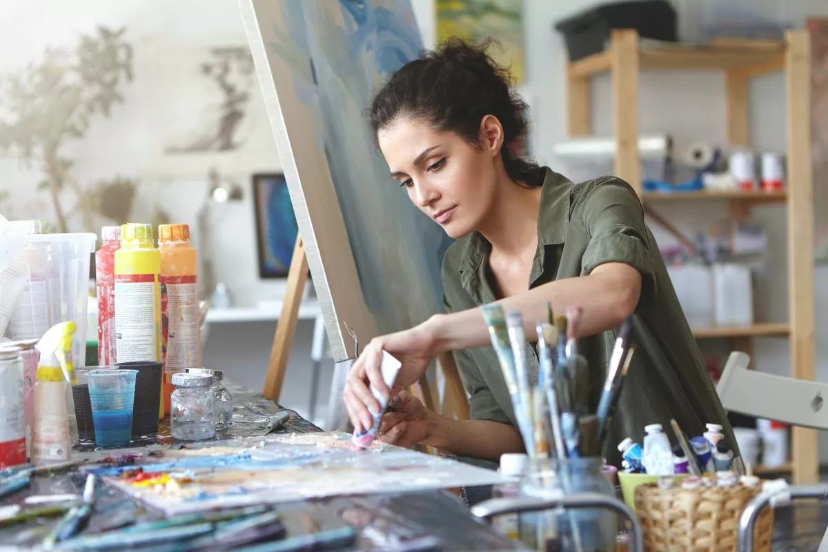 Une femme travaillant sur une toile dans un atelier d'art, avec la tranquillité de savoir qu'elle recevra les allocations du travailleur artiste.