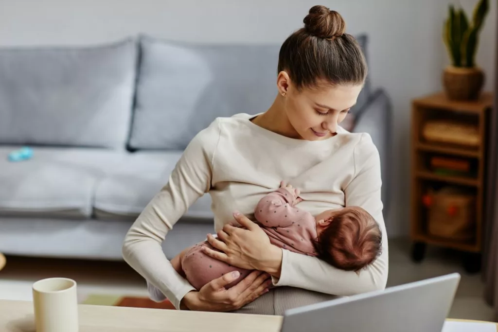 Une mère embrasse son bébé pendant qu'elle travaille avec son ordinateur portable durant sa pause pour allaiter le bébé.