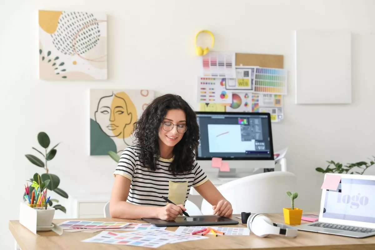 Une femme assise à un bureau avec un ordinateur portable et une tablette à dessin, illustrant le concept des "Pensions complémentaires d’indépendants".