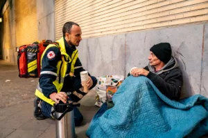 Un homme sans-abri sous une couverture reçoit l'aide d'un secouriste de la Croix-Rouge. L'attestation de sans-abri pourrait l'aider à trouver un logement.