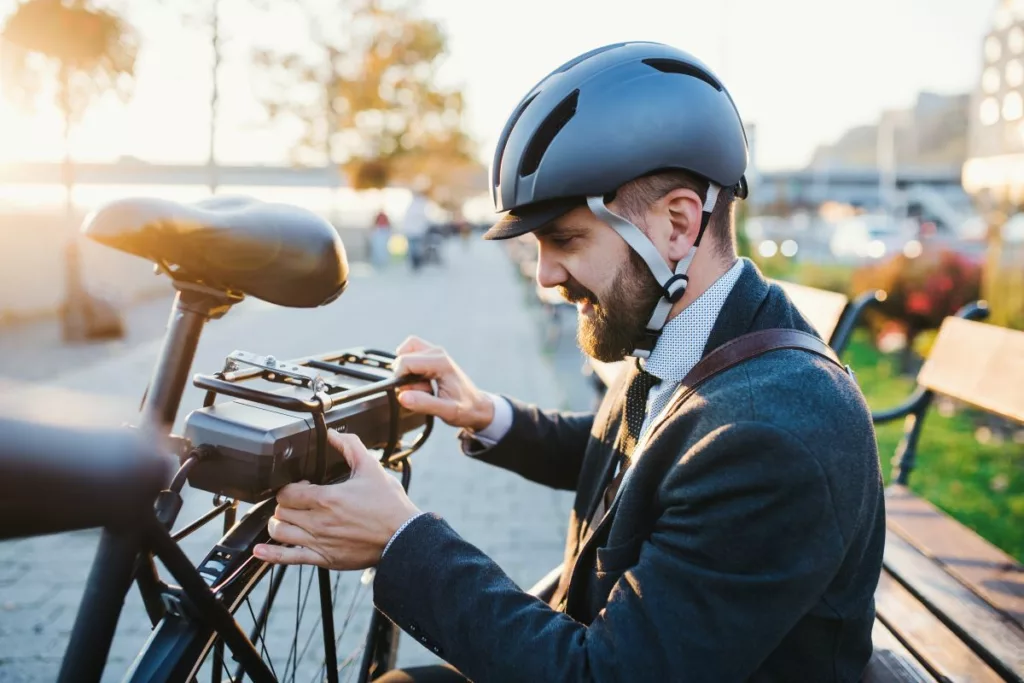 Un homme souriant avec un casque ajuste son vélo électrique, bénéficiant des aides à la mobilité pour les vélos électriques.