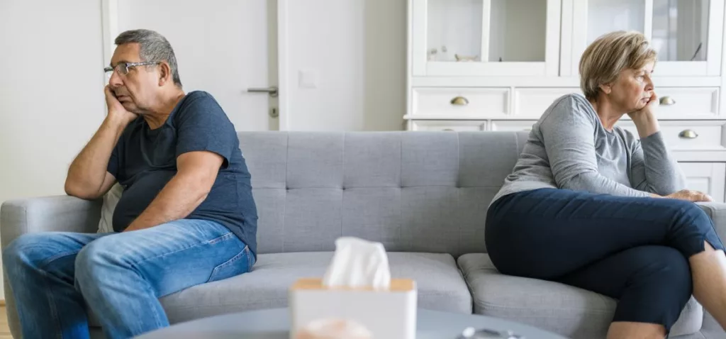 Un couple de personnes âgées assises sur un canapé, regardant dans des directions opposées avec un air préoccupé, illustrant le sujet de la "Pension de   conjoint divorcé" en Belgique.