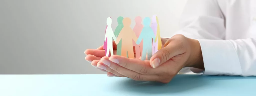 Des mains ouvertes tenant des silhouettes colorées en papier représentant des personnes. Cette image symbolise le rôle protecteur et solidaire des assistantes sociales, mettant l'accent sur le soutien communautaire et l'aide individuelle offerte par les services sociaux.