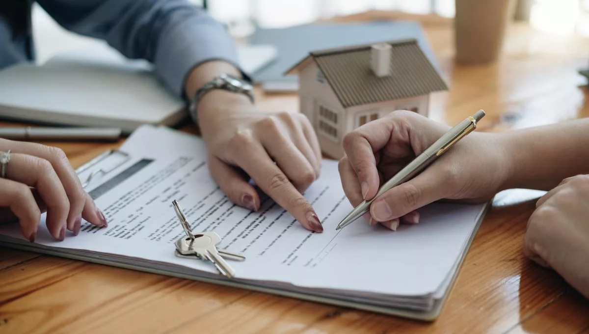 Deux personnes signant un contrat de bail, avec des clés et une maquette de maison sur la table, illustrant la nouvelle législation sur les baux à Bruxelles en 2024.