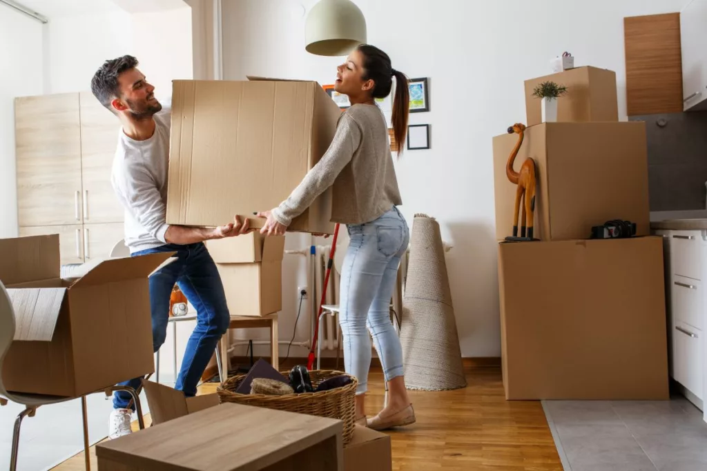 Un couple porte des cartons dans un nouvel appartement, entouré de boîtes de déménagement. Cette image illustre les aides au déménagement en Belgique.