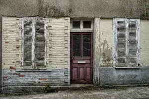 Façade d'une maison ancienne et délabrée avec volets et porte en mauvais état. Cette image illustre les conditions pouvant donner droit à l'Allocation de relogement en Belgique.