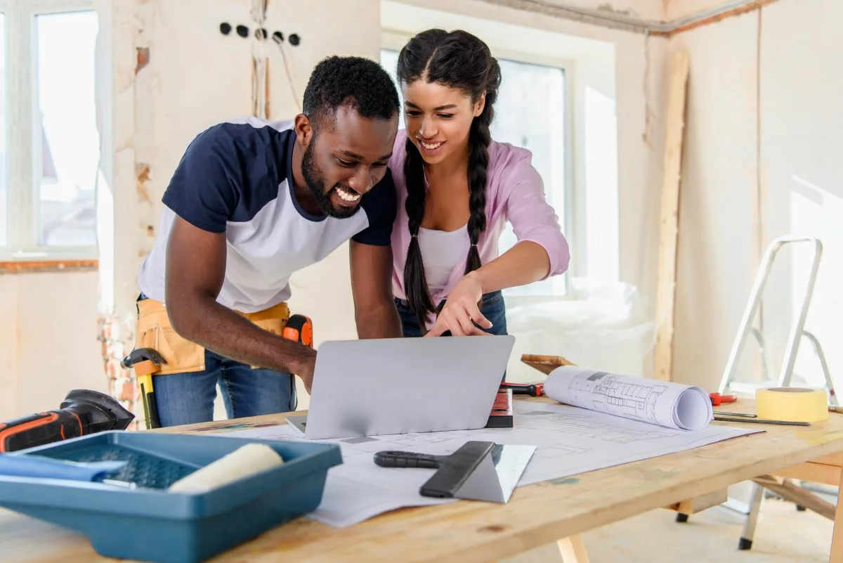 Un couple planifiant des rénovations sur un ordinateur dans un chantier, illustrant les aides financières disponibles grâce aux primes habitation en Belgique.