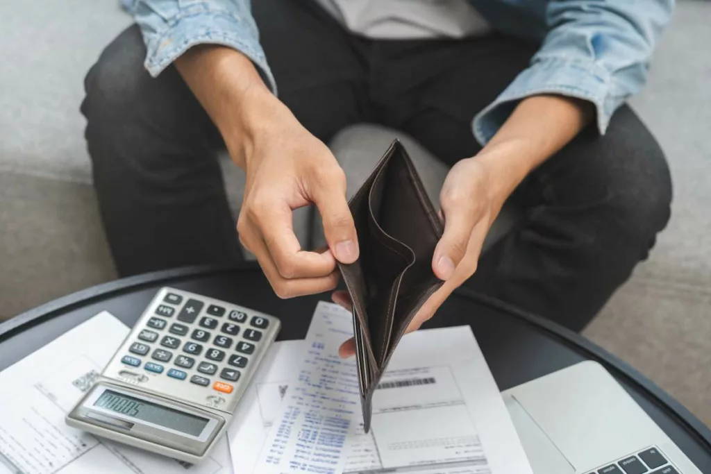 Personne montrant un porte-monnaie vide, symbolisant les difficultés financières, en lien avec l'Aide Sociale Équivalente (ASE) pour les bénéficiaires de soutien financier.