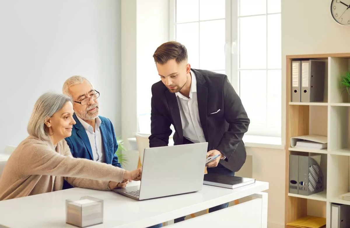 Conseiller RH expliquant le dispositif Impulsion 55+ à un couple de demandeurs d'emploi seniors dans un bureau lumineux en Wallonie.