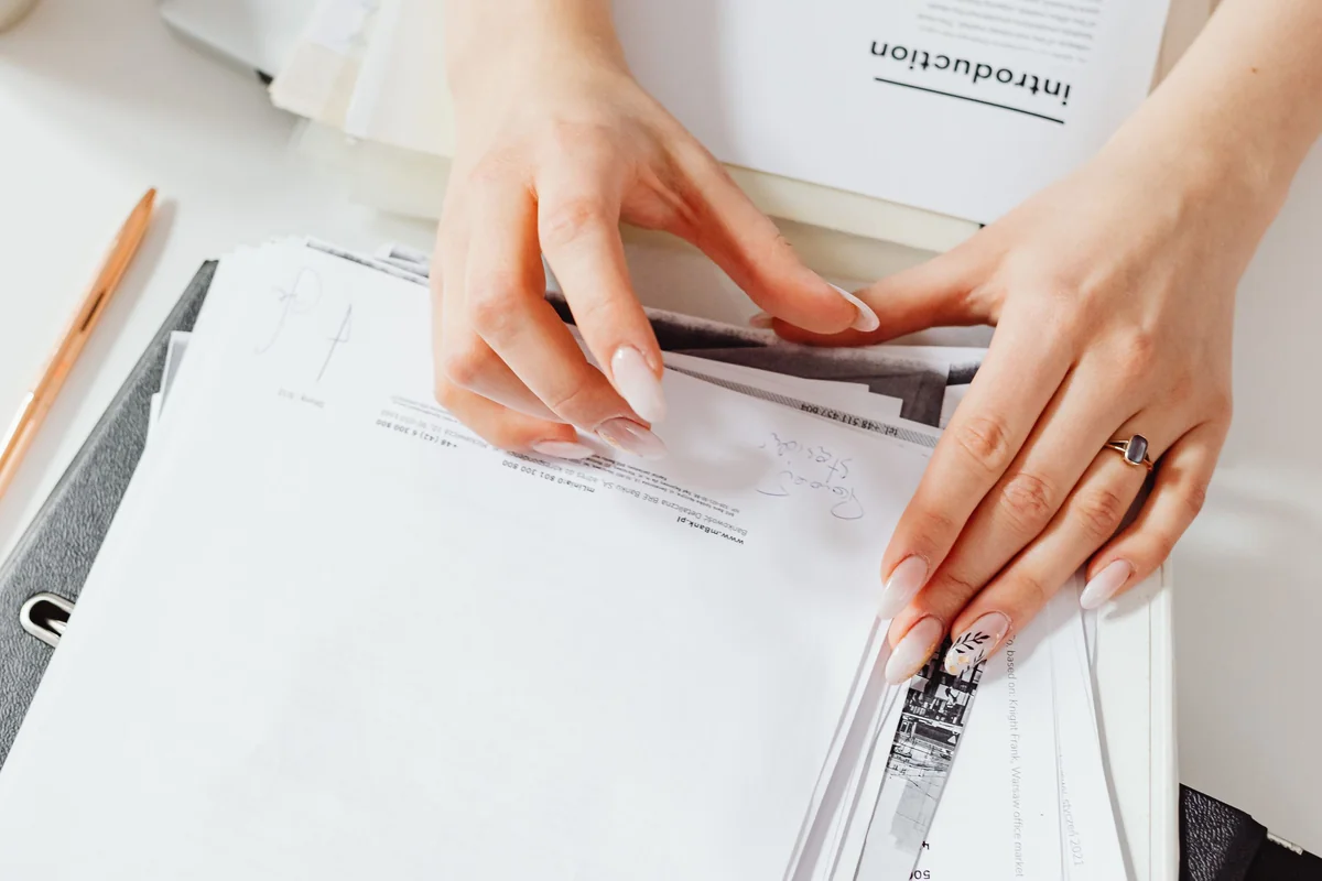 Gros plan sur des mains qui rangent des documents dans un classeur, avec un crayon sur le bureau.